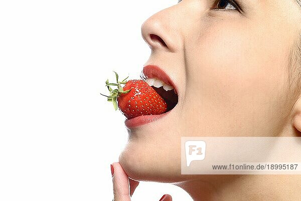 Schöne Frau mit sinnlichen roten Lippen ißt eine üppige reife rote frische Erdbeere mit ihren Lippen in Erwartung des Leckerbissen gescheitelt  Nahaufnahme Teilansicht ihres Gesichts vor weißem Hintergrund