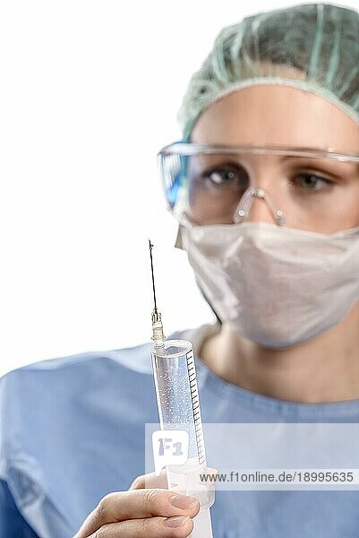Nahaufnahme der Hände einer Ärztin  die einen blaün Arztkittel  eine Schutzmaske und eine Schutzbrille trägt  während sie die Luft aus einer mit einem flüssigen Medikament gefüllten Spritze entfernt  um eine Embolie zu verhindern