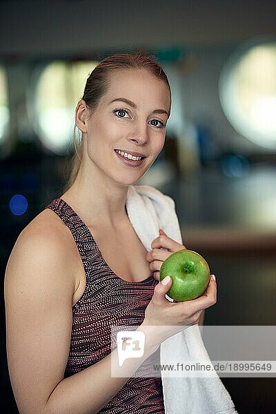 Attraktive  natürliche  junge Sportlerin  die einen frischen  knackigen  grünen Apfel in der Hand hält und mit einem ruhigen Lächeln in die Kamera blickt  in einem Konzept für gesunde Ernährung