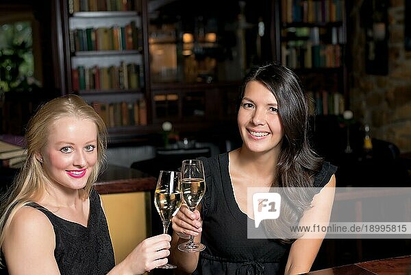Zwei schöne elegante Frauen Freunde in stilvollen einfachen schwarzen Cocktailkleider Toast einander mit Gläsern von gekühlten Champagner  wie sie auf eine Nacht zusammen feiern
