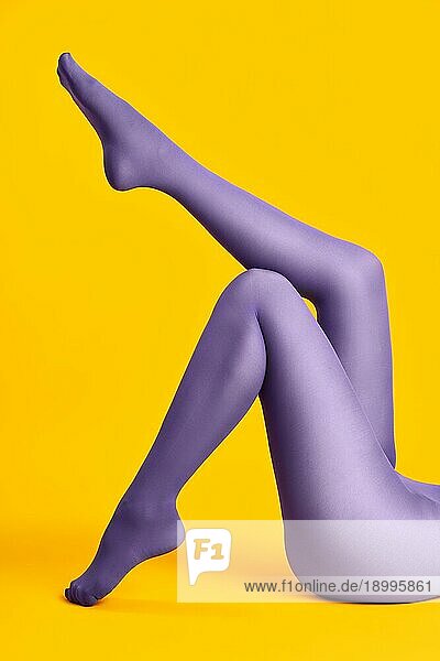 Lange schlanke Beine der schönen jungen Frau in hellen Strumpfhosen entspannen auf gelbem Hintergrund