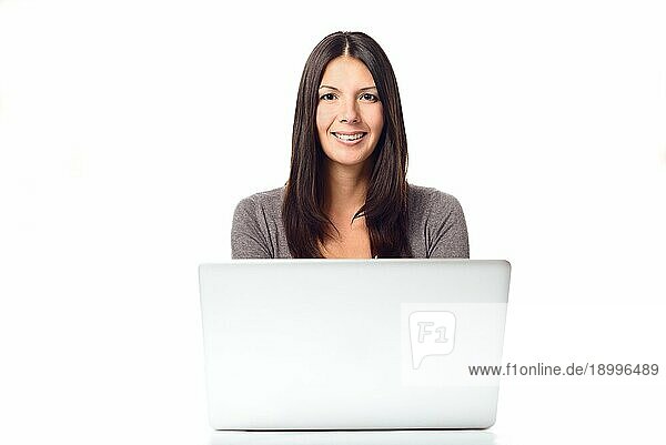 Glückliche junge Frau mit langen Haaren  die mit ihrem Laptop beschäftigt ist und in die Kamera schaut  vor weißem Hintergrund