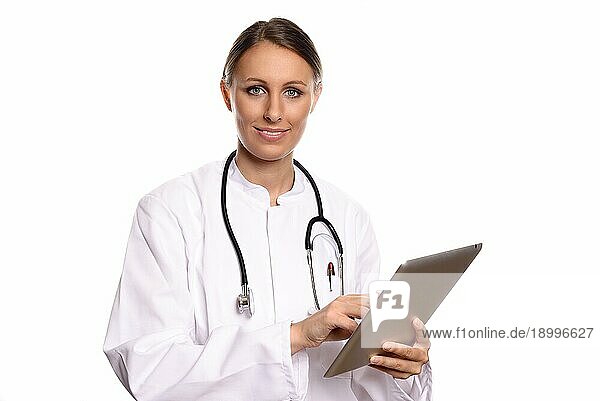 Attraktive weibliche Krankenschwester oder Ärztin in einem weißen Kittel stehend  die einen Tabletcomputer konsultiert und die Informationen mit einem freundlichen Ausdruck liest  vor weißem Hintergrund