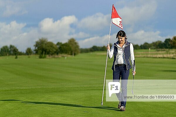 Eine Golferin hält die Fahne des Lochs in der Hand  als sie sie entfernt  um ihren letzten Putt auf dem Grün zu machen  und lächelt in die Kamera