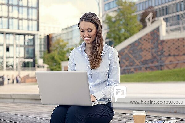 Attraktive junge Frau in formeller Kleidung bei der Arbeit im Freien an einem Laptop  mit einer drahtlosen Verbindung zum Internet  an einem schönen Sommertag