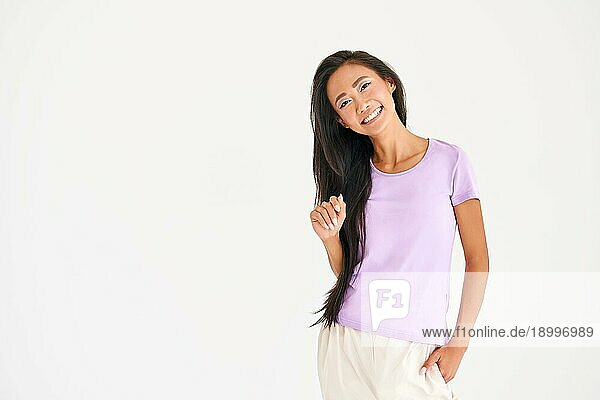 Hübsche lächelnde asiatische Frau in lässiger Kleidung posiert mit Blick in die Kamera auf weißem Hintergrund mit Kopie Raum