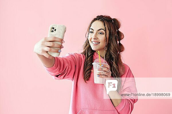 Junge trendige Frau macht Selfie Porträt hält Milchshake auf rosa Hintergrund. kreatives Konzept