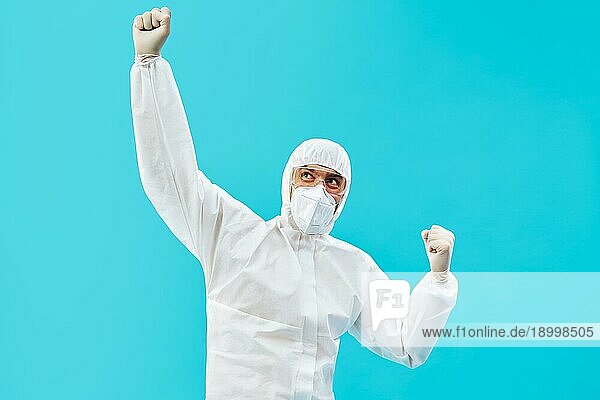 Glücklicher Arzt in PSA Anzug feiert seinen Erfolg mit Siegergeste und Hände hoch auf blauem Hintergrund. Sieg  Triumph und Emotionen Konzept