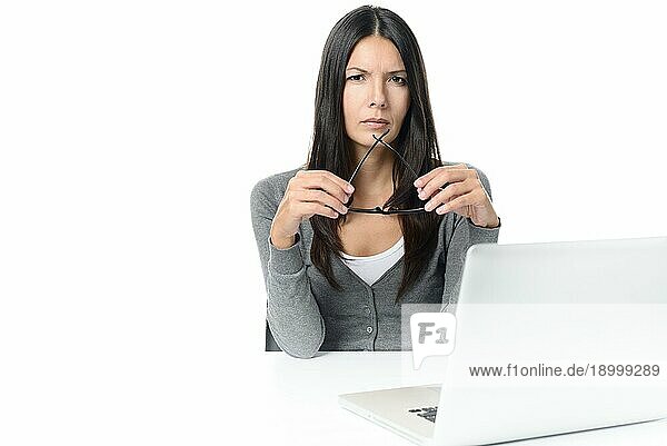 Seriöse junge Frau mit langen Haaren  die an ihrem Laptop arbeitet  mit einer Brille in der Hand  vor weißem Hintergrund