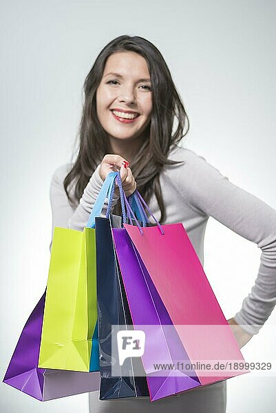 Schöne zufriedene Frau  die eine Reihe von bunten Einkaufstaschen hält und glücklich über ihren erfolgreichen Einkaufsbummel lächelt  slektiver Fokus