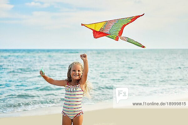 Glückliches kleines Mädchen mit fliegendem Drachen am tropischen Strand. Strand Spaß  Kindheit Konzept