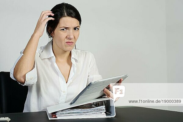 Eine verwirrte Frau kratzt sich am Kopf und zieht eine Grimasse  während sie versucht  eine Antwort auf ein Problem zu finden  das ihr auf ihrem Tabletcomputer gestellt wurde