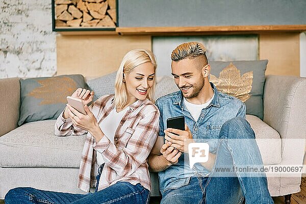 Lächelndes junges Paar entspannt sich auf der Couch mit Smartphone zu Hause. Glücklich zusammen