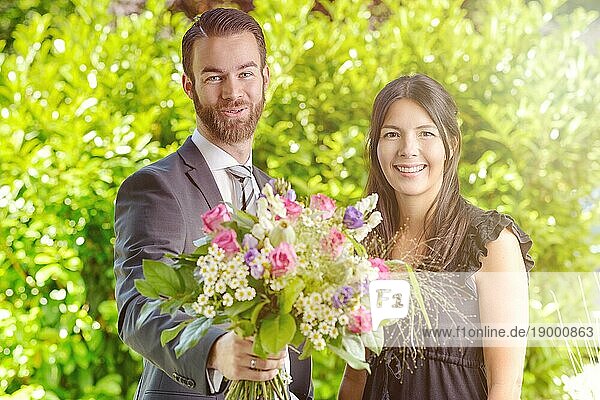 Glückliches junges Paar im Garten mit einem Strauß verschiedener frischer Blumen  lächelt in die Kamera