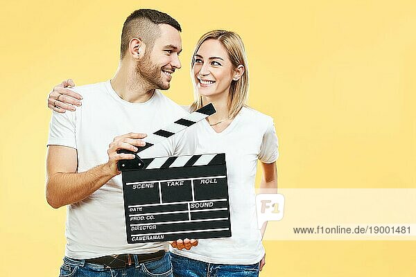 Junges glückliches Paar mit Kinoklappe auf gelbem Hintergrund. Spaß  Kinematographie Konzept
