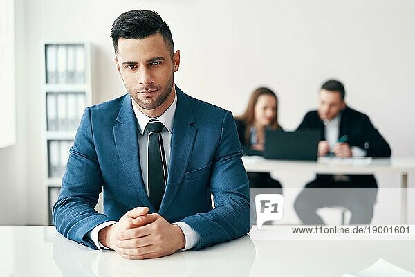Porträt der zuversichtlich  gut aussehend Geschäftsmann sitzt im Büro mit seinem Businessteam auf dem Hintergrund. Führung und Erfolg Konzept