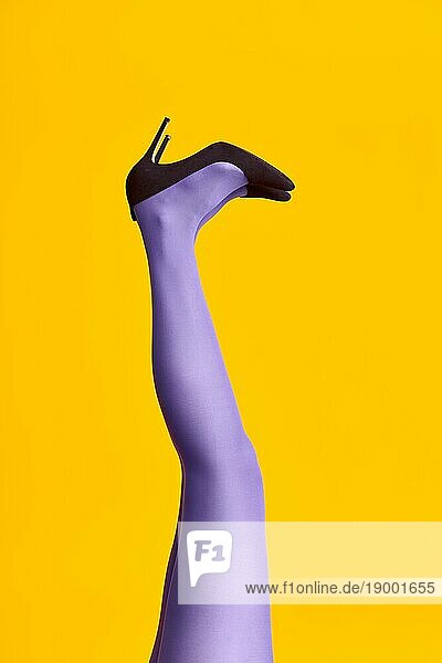 Hochgezogene Frauenbeine in hellen Strumpfhosen und stilvollen hochhackigen Schuhen auf gelbem Hintergrund. Entspannung  Glamour  Pop Art Konzept