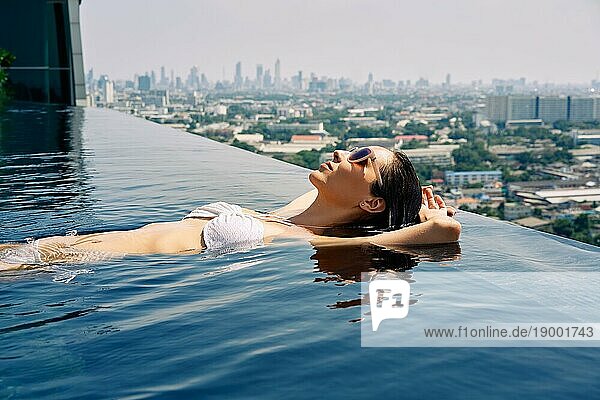 Junge Frau entspannt sich am Rande des Dachterrassenpools. Sommerurlaub Konzept