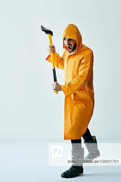 Aggressiver Mann in orangefarbenem Regenmantel droht mit Axt. Emotionen Konzept