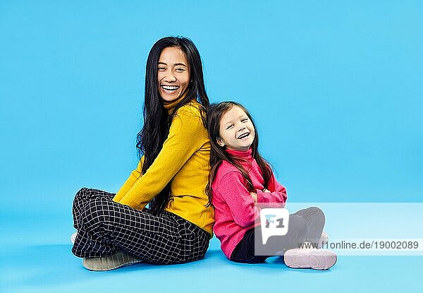 Glückliche lächelnde Mutter und ihre kleine süße Tochter posieren auf blauem Studio Hintergrund