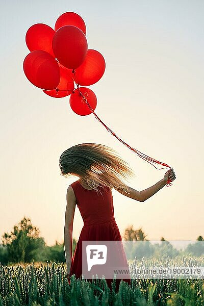 Junge Frau schüttelt den Kopf  ihre Haare fliegen um sie herum und sie hält rote Luftballons