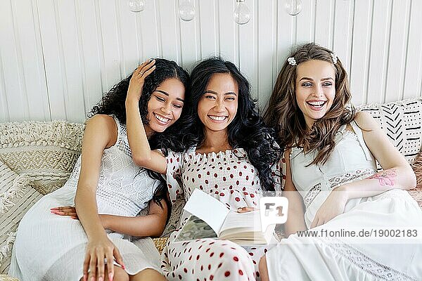 Lächelnde multiethnische Mädchen haben Spaß zusammen  Buch lesen und genießen Sie zu Hause Partei im Inneren des Wohnmobils. Frauen Freundschaft und Frauen Schönheit Konzept