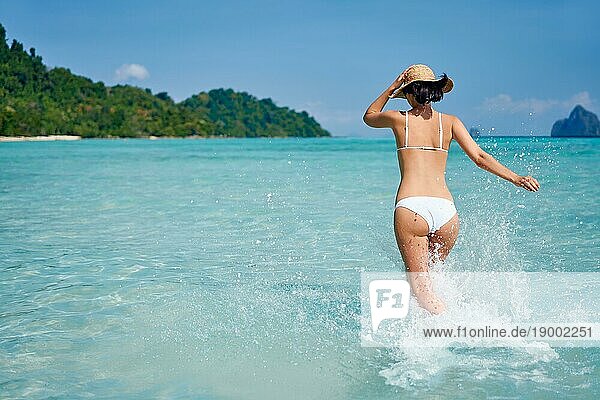 Glückliche schlanke Frau  die ins Meer läuft  genießt ihren tropischen Strandurlaub  hat Spaß und spritzt Wasser mit Kopierraum. Sommer entspannen  Reisekonzept