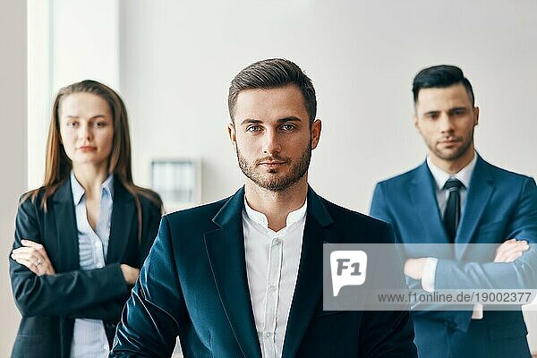 Porträt von zuversichtlich  gut aussehend Geschäftsmann im Büro mit seinem Team auf dem Hintergrund. Führung und Erfolg Konzept