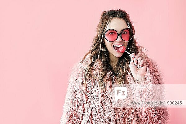 Modeporträt einer hübschen Hipster Frau  die einen Lutscher hält und in die Kamera schaut  auf rosa Hintergrund mit Kopierraum