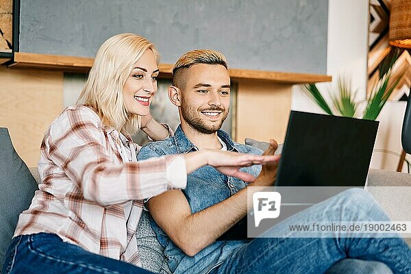 Fröhliches junges Paar mit Laptop  das im Internet surft und zu Hause auf dem Sofa sitzt