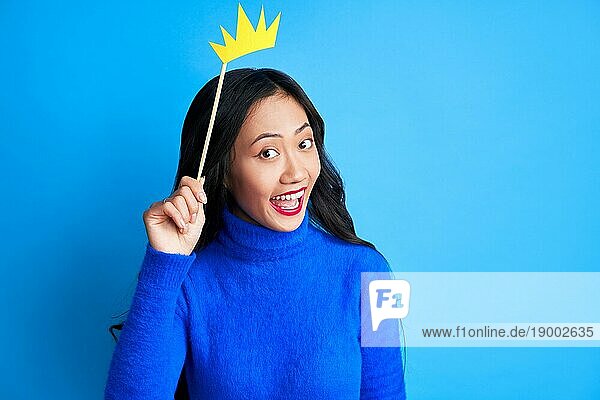 Emotionale überraschte Frau mit Papierkrone auf Stock auf blauem Hintergrund. Party  Emotionen Konzept