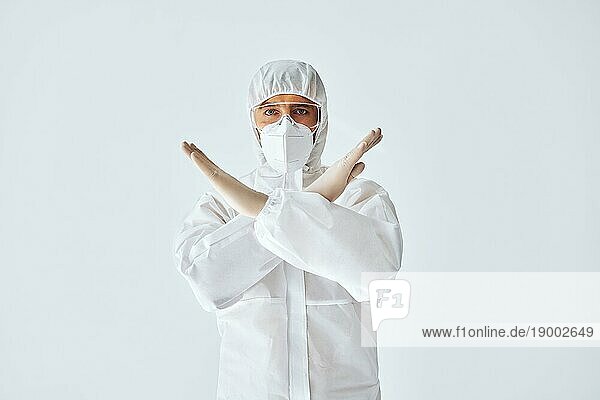 Arzt im medizinischen Schutzanzug zeigt Stoppschild auf weißem Hintergrund. Verbotssymbol