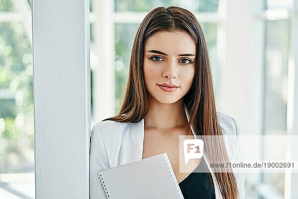 selbstbewusste Geschäftsfrau  die Dokumente in der Hand hält und in die Kamera schaut  in einem modernen Kreativbüro mit Kopierraum