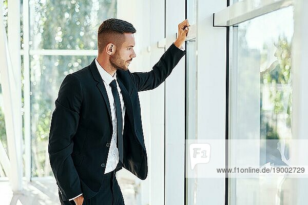 Profilansicht eines selbstbewussten Geschäftsmannes in einer eleganten Suite in einem modernen  kreativen Büro mit Blick durch die Panoramafenster