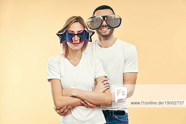 Junges glückliches Paar in lustiger Partybrille auf beigem Hintergrund. Spaß Konzept