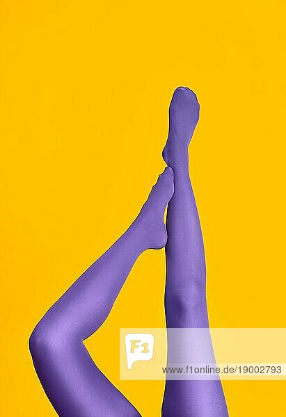 Schlanke weibliche Beine in lila Strumpfhosen auf hellgelbem Hintergrund angehoben