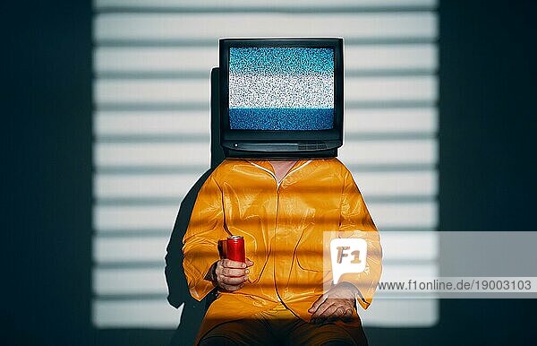 Surreale Kunst der TV süchtigen Männchen mit Fernseher statt Kopf. Medien Zombie Konzept mit männlichen in leuchtend gelben Regenmantel hält süße Soda in einer roten Dose in der Hand und posiert auf Studio in Lichter Schatten