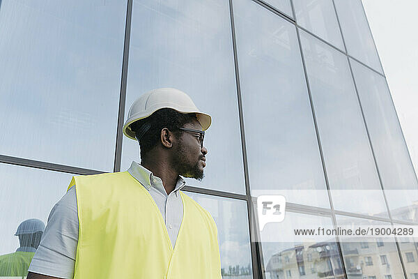 Engineer in reflective clothing waiting in front of glass building