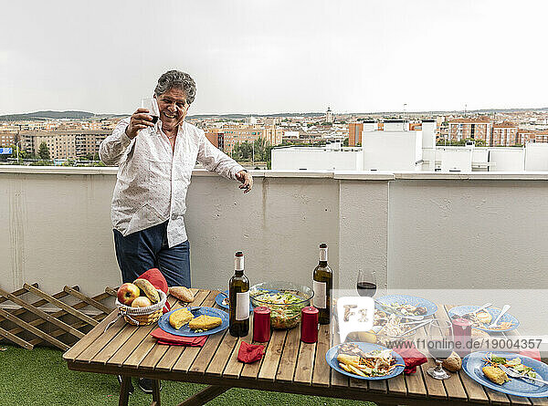 Happy senior man holding wineglass with food on table in balcony