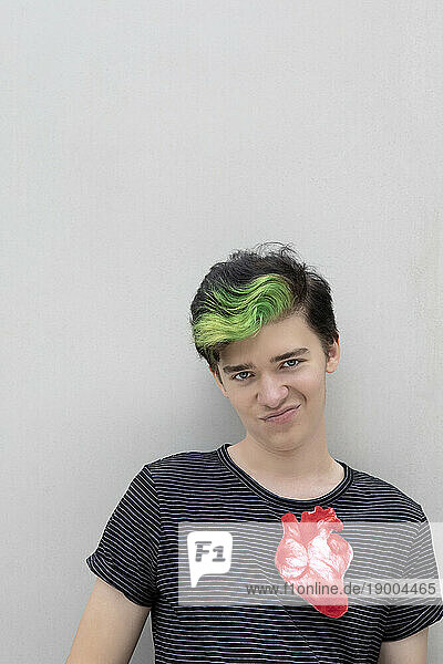 Teenage boy with dyed green hair and artificial heart against gray background