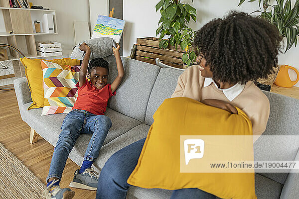 Happy boy playing pillow fight with mother on sofa at home