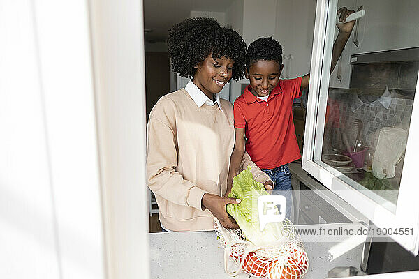 Happy mother and son with groceries standing by kitchen counter at home