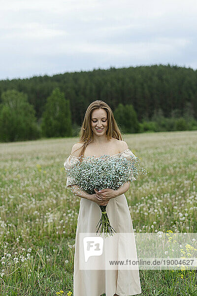 Smiling young woman holding flower bouquet on field
