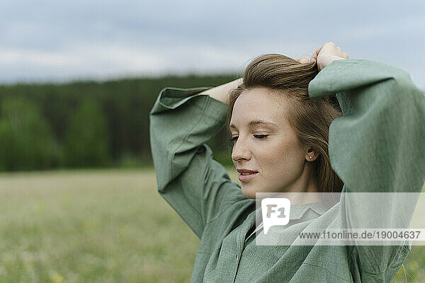 Beautiful young woman tying hair on field