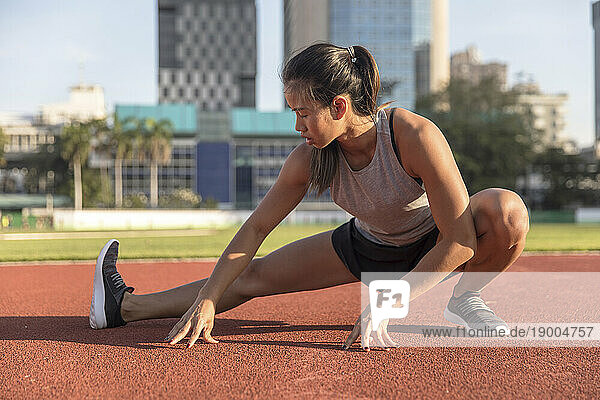 Young woman doing leg exercise in sports field