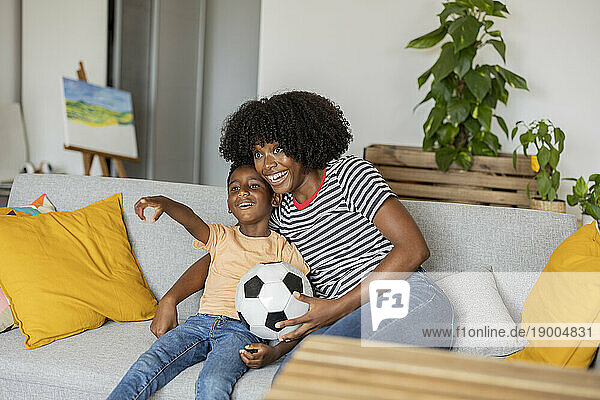 Happy mother with boy gesturing and sitting on sofa at home