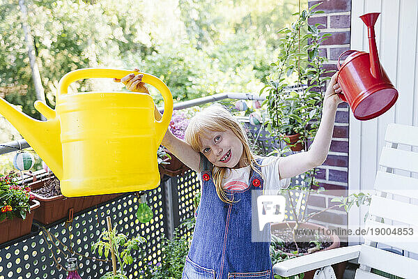 Smiling girl standing with watering cans in balcony