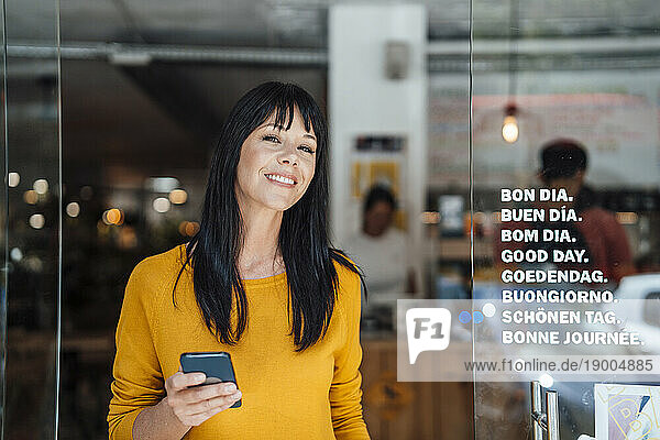 Happy mature woman standing with mobile phone in doorway