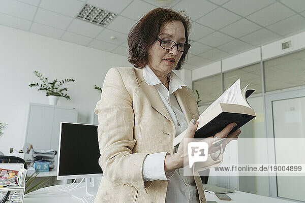 Senior businesswoman reading book standing in office