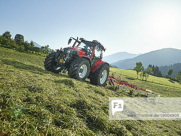 Farmer using tractor and mowing grass field near mountain